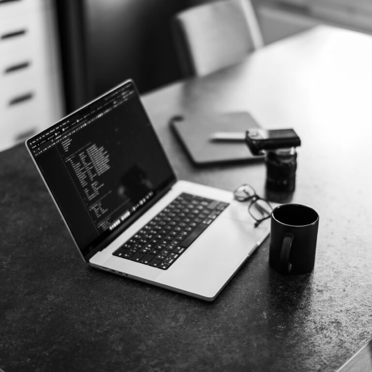 Home Black-and-white photo of a laptop on a table with coffee, perfect for remote work themes.