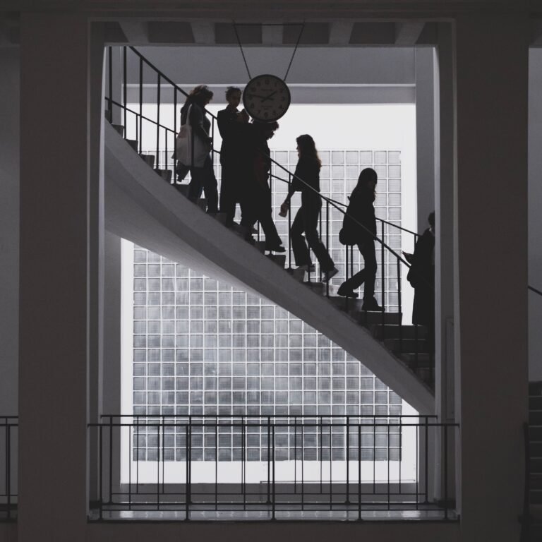 Home Silhouetted people ascending a modern staircase in a bright office building.